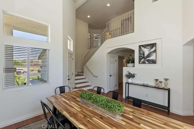 dining space featuring baseboards, arched walkways, stairway, wood finished floors, and a high ceiling