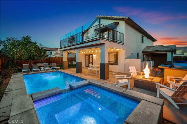 back of property at dusk featuring a patio, fence, a balcony, and stucco siding