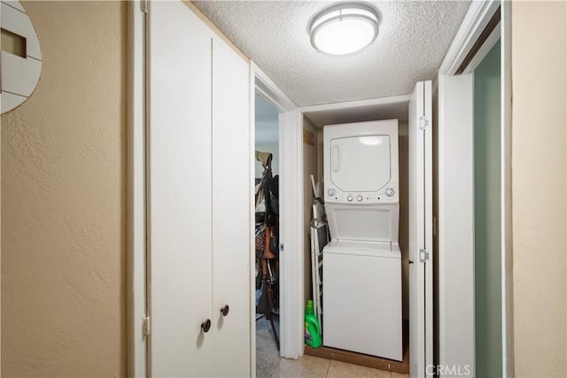 laundry room with stacked washer and clothes dryer, a textured wall, a textured ceiling, and laundry area