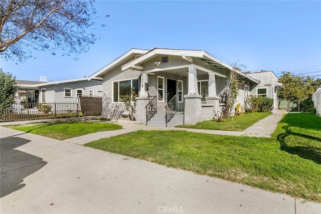 bungalow-style house with a fenced front yard, a front lawn, and stucco siding