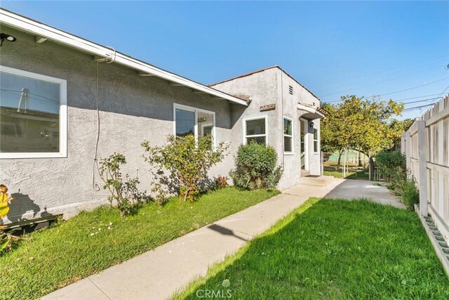 view of property exterior featuring a patio, a lawn, fence, and stucco siding