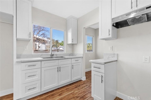 kitchen with light countertops, white cabinets, a sink, under cabinet range hood, and baseboards