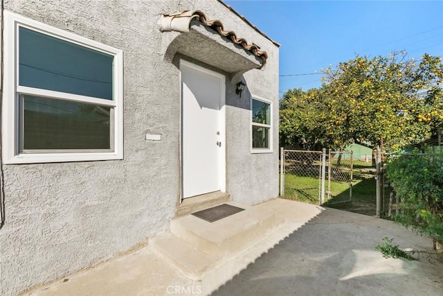 property entrance featuring a patio area, fence, and stucco siding