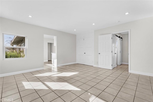 unfurnished bedroom with light tile patterned floors, recessed lighting, a closet, a barn door, and baseboards