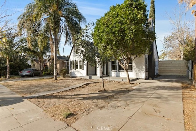 view of property hidden behind natural elements featuring concrete driveway and fence