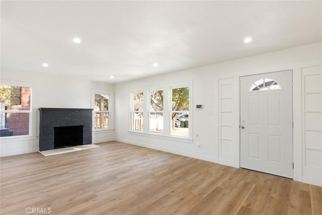 entryway with light wood-style floors, recessed lighting, a brick fireplace, and baseboards