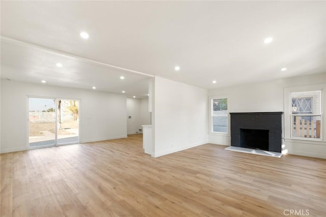 unfurnished living room featuring recessed lighting, a fireplace with raised hearth, and light wood-style flooring