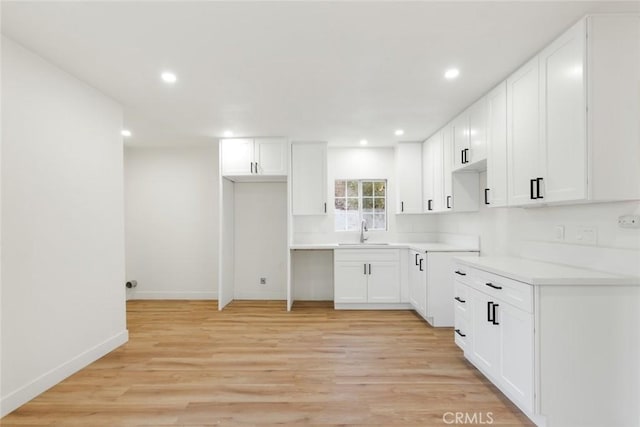 kitchen featuring light countertops, light wood-type flooring, a sink, and white cabinetry