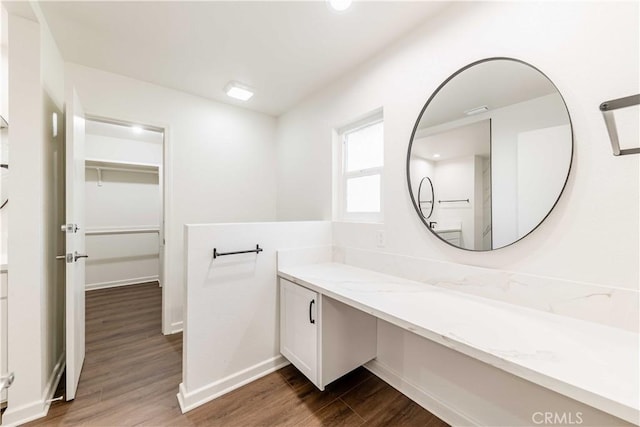 bathroom with vanity, wood finished floors, a walk in closet, and baseboards