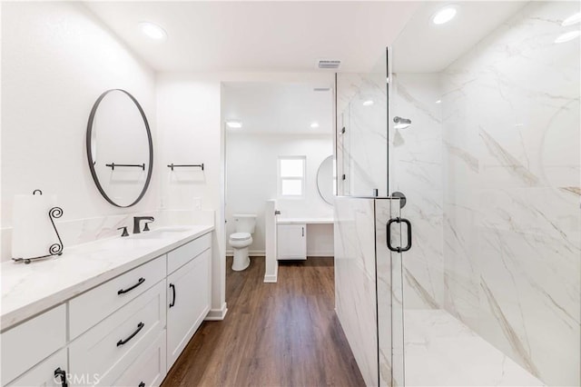 bathroom featuring toilet, a marble finish shower, wood finished floors, and vanity