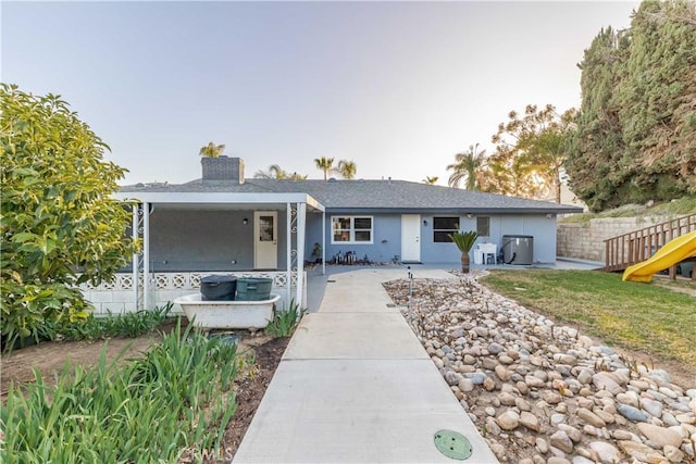 ranch-style home with a chimney, a playground, fence, and stucco siding