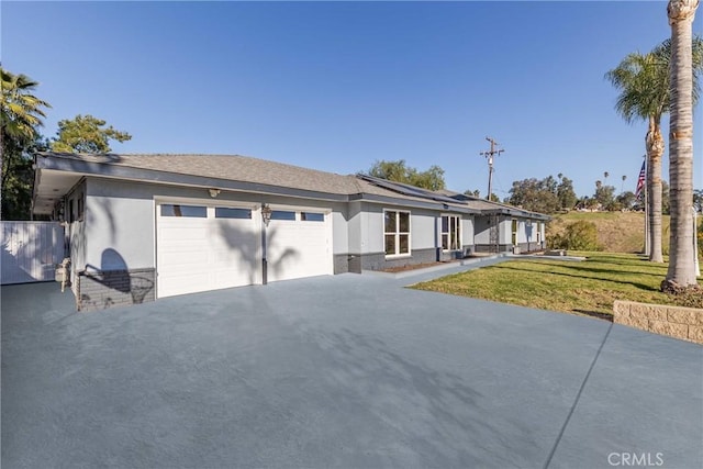 view of front of property featuring a garage, solar panels, driveway, stucco siding, and a front yard