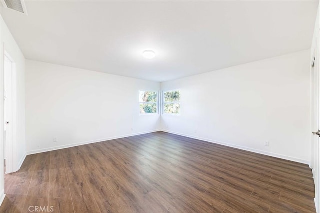 unfurnished room featuring dark wood-style flooring, visible vents, and baseboards