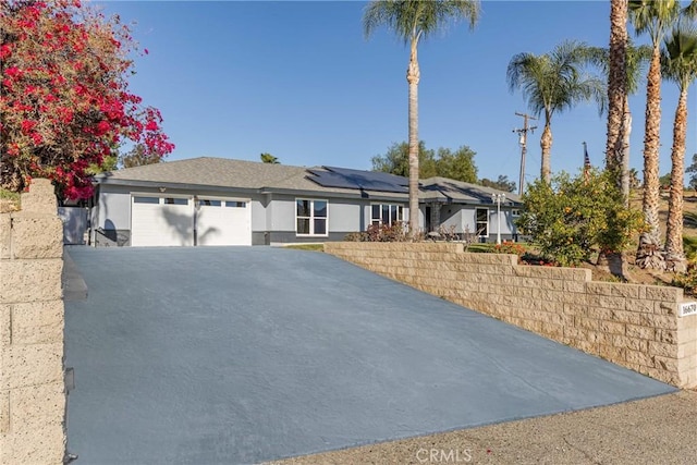 ranch-style house with stucco siding, driveway, an attached garage, and solar panels