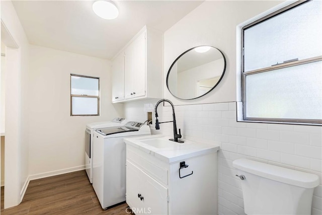 washroom with dark wood-style flooring, tile walls, washing machine and clothes dryer, a sink, and laundry area