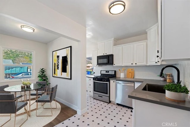 kitchen featuring dark countertops, appliances with stainless steel finishes, backsplash, white cabinetry, and a sink