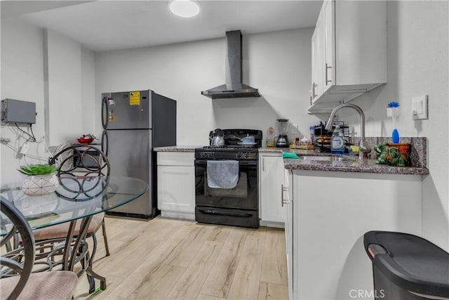 kitchen featuring white cabinetry, a sink, wall chimney range hood, dark stone counters, and black appliances