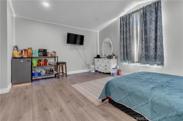 bedroom with wood finished floors, freestanding refrigerator, and baseboards