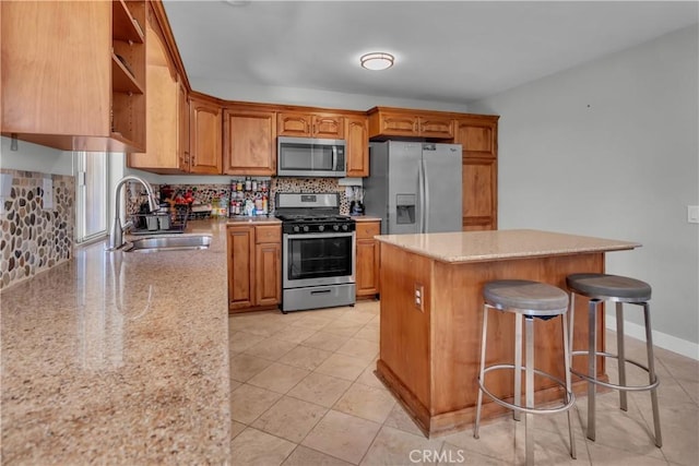 kitchen with a center island, brown cabinets, stainless steel appliances, a sink, and light stone countertops