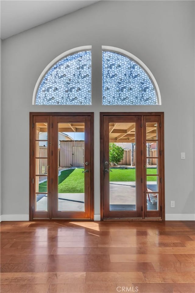 doorway with french doors, a towering ceiling, baseboards, and wood finished floors