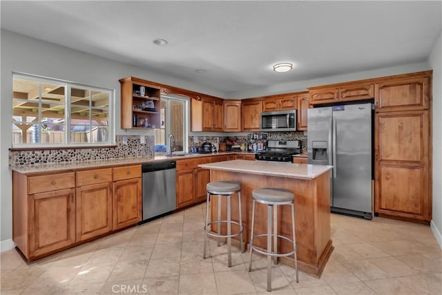 kitchen with brown cabinets, light countertops, appliances with stainless steel finishes, a kitchen island, and a sink