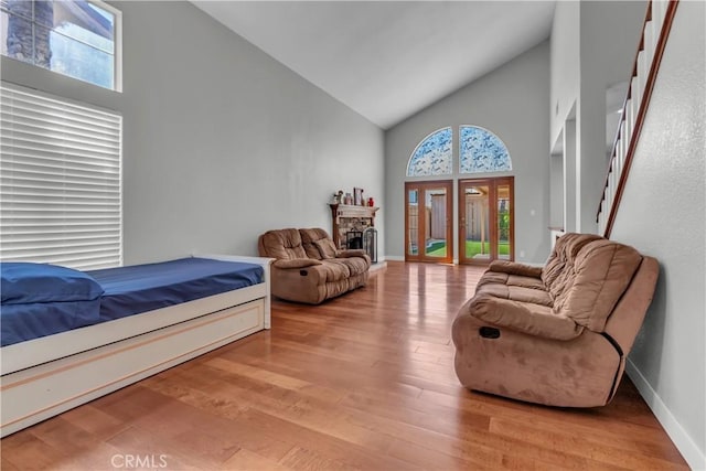 bedroom with a stone fireplace, multiple windows, light wood-style flooring, and access to exterior