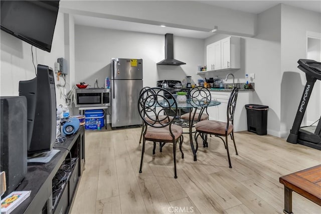 kitchen featuring dark countertops, wall chimney exhaust hood, light wood-style flooring, appliances with stainless steel finishes, and white cabinetry