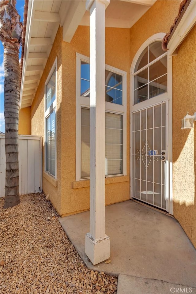 property entrance featuring a patio area, fence, and stucco siding