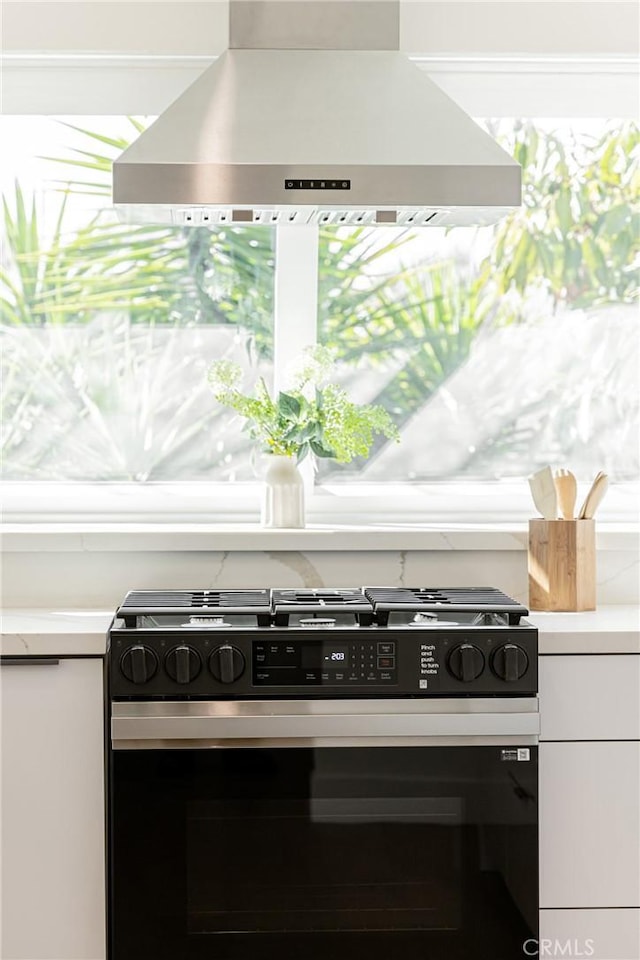 interior details with white cabinetry, extractor fan, light countertops, and gas stove