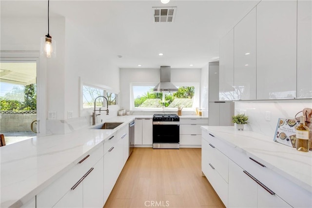 kitchen with wall chimney exhaust hood, modern cabinets, a sink, and gas stove