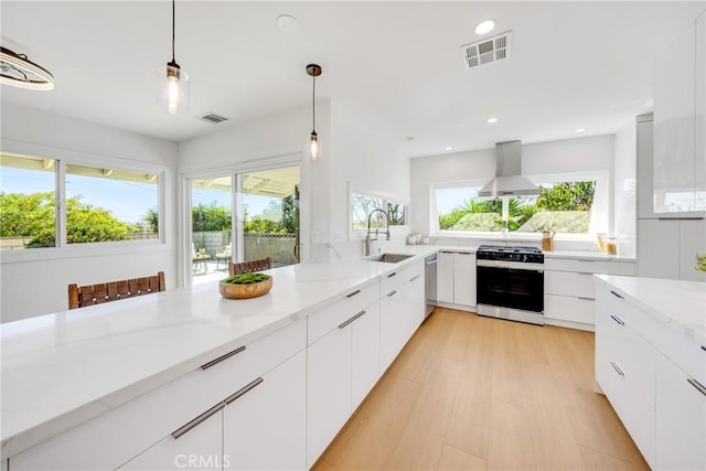 kitchen featuring wall chimney range hood, a sink, gas range, visible vents, and modern cabinets