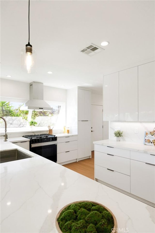 kitchen with range with gas stovetop, visible vents, a sink, modern cabinets, and wall chimney exhaust hood