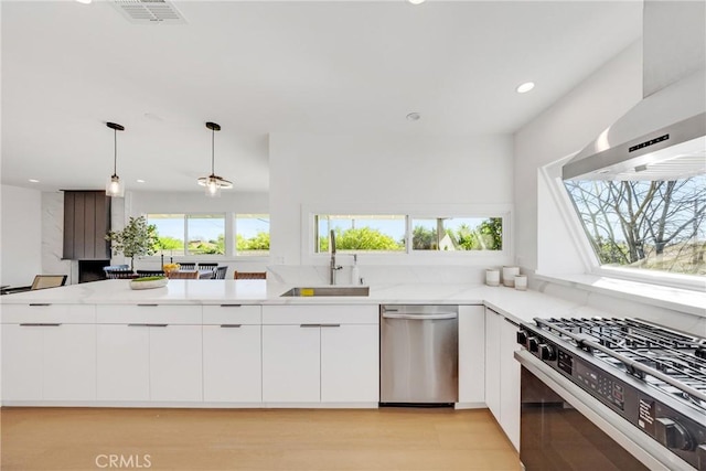 kitchen featuring visible vents, wall chimney exhaust hood, white cabinetry, a sink, and appliances with stainless steel finishes
