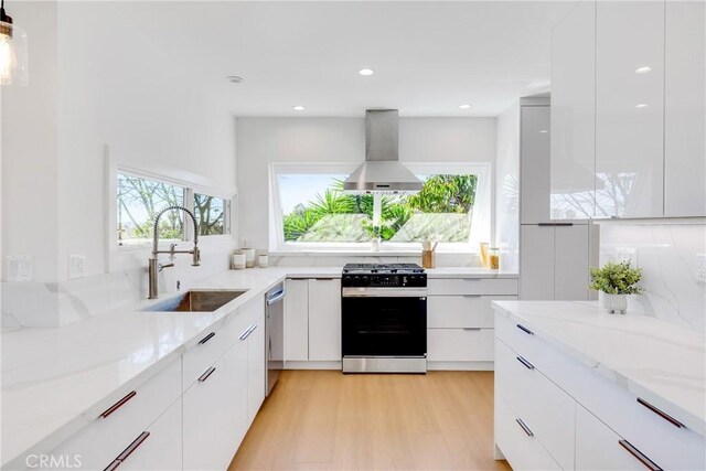 kitchen with stainless steel dishwasher, modern cabinets, gas range, wall chimney exhaust hood, and a sink