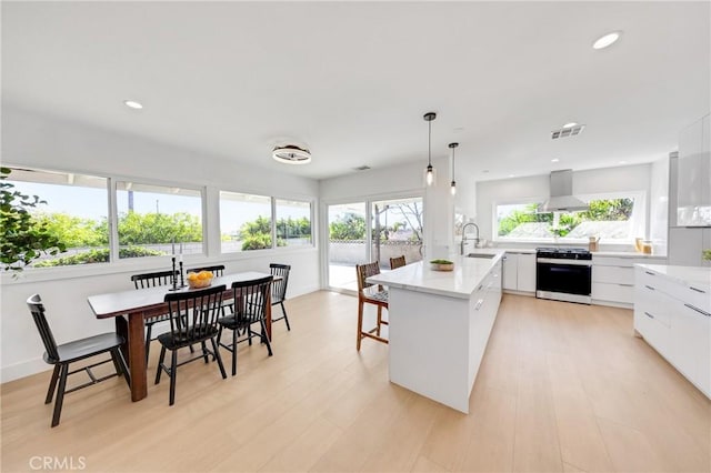 kitchen featuring a sink, visible vents, wall chimney range hood, modern cabinets, and range with gas cooktop