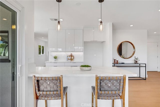 kitchen featuring a kitchen breakfast bar, modern cabinets, visible vents, and white cabinets