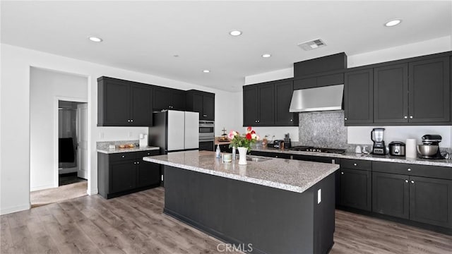 kitchen featuring stainless steel appliances, visible vents, a sink, light stone countertops, and under cabinet range hood