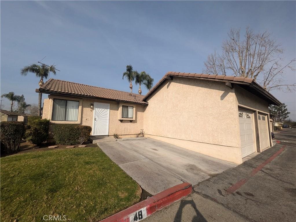 view of front of property featuring a garage, a front yard, a tiled roof, and stucco siding