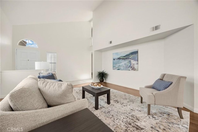 living area with visible vents, a towering ceiling, baseboards, and wood finished floors