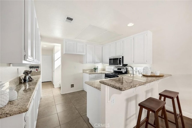 kitchen featuring light stone counters, a breakfast bar area, visible vents, white cabinetry, and appliances with stainless steel finishes