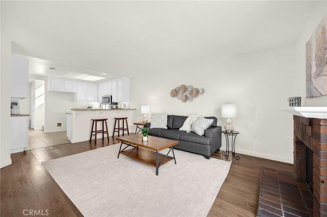 living room with a brick fireplace, wood finished floors, and baseboards