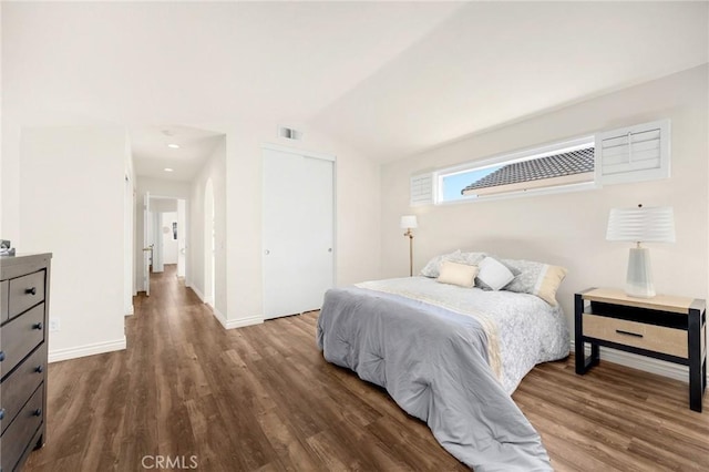 bedroom featuring dark wood-style flooring, visible vents, baseboards, vaulted ceiling, and a closet