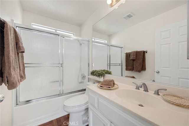 full bathroom featuring toilet, visible vents, bath / shower combo with glass door, and vanity