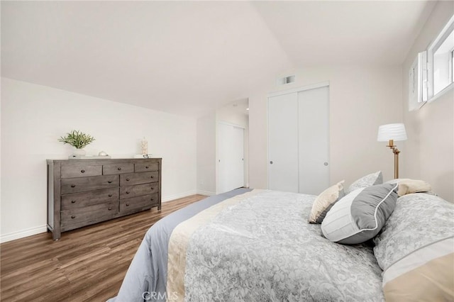 bedroom featuring two closets, lofted ceiling, visible vents, wood finished floors, and baseboards