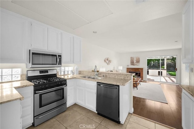 kitchen featuring a peninsula, a sink, white cabinetry, open floor plan, and appliances with stainless steel finishes