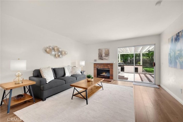 living room featuring a brick fireplace, baseboards, and wood finished floors