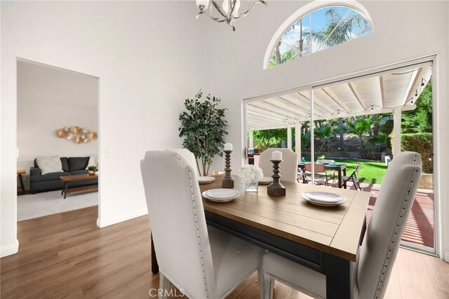 dining space with an inviting chandelier, a high ceiling, baseboards, and wood finished floors