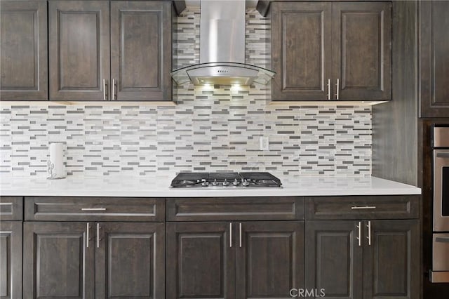 kitchen with dark brown cabinets, wall chimney range hood, light countertops, and appliances with stainless steel finishes