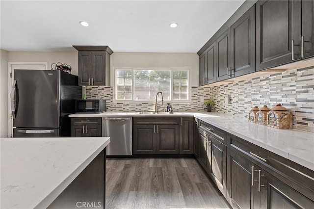 kitchen with tasteful backsplash, light stone counters, wood finished floors, stainless steel appliances, and a sink