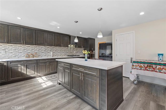 kitchen featuring light wood-type flooring, light countertops, dark brown cabinets, and oven